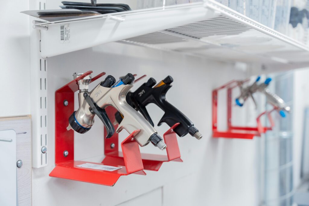Three spray guns neatly organized on red wall mounts in a well-lit workshop setting.